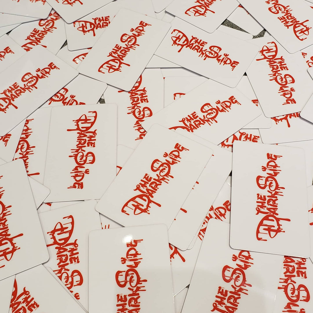 A pile of white gift cards featuring the words 'THE DARK SLIDE' printed in a red stylized font.