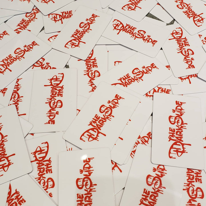 A pile of white gift cards featuring the words 'THE DARK SLIDE' printed in a red stylized font.