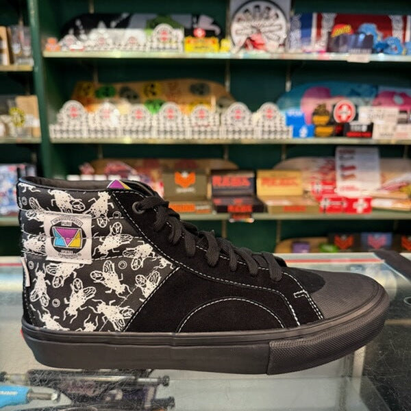 A black high-top sneaker with white graphic patterns on the heel panel, displayed on a glass counter inside a retail store.