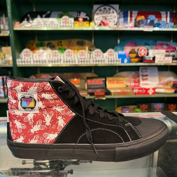 A high-top sneaker with a black leather upper, black laces, and a red side panel decorated with a white butterfly pattern, displayed on a glass counter in a retail store.