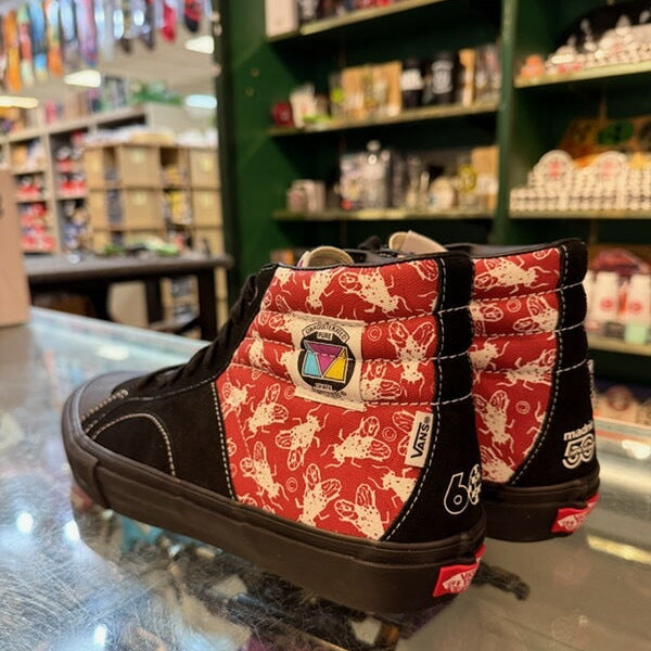 A pair of Vans high-top sneakers with a red and white bunny print canvas and black suede overlays, displayed on a glass counter inside a retail store.