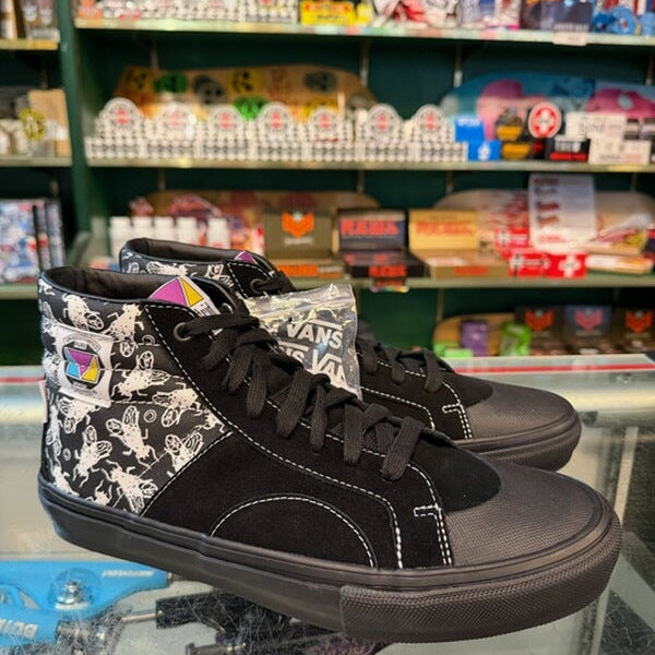 A pair of black high-top sneakers with white graphic patterns on the sides, displayed on a glass counter inside a retail store.