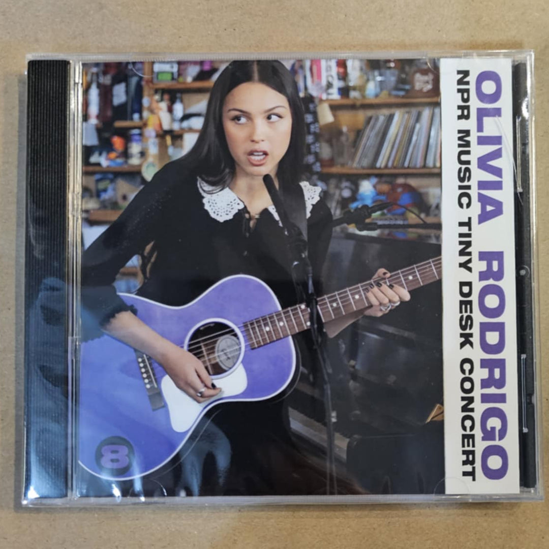 CD cover of Olivia Rodrigo's 'Tiny Desk Concert' with a person holding a guitar on a beige background