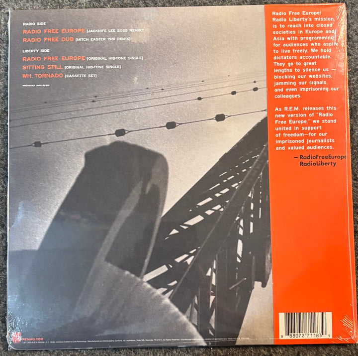 The back cover of R.E.M. - Radio Free Europe 2025 featuring a black and white photograph of a bridge and a large orange band on the right side with text and a barcode.