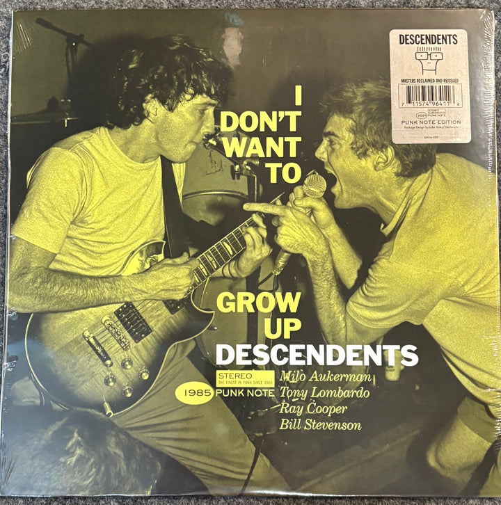 A vinyl record sleeve for the band Descendents' album 'I Don't Want To Grow Up' (1985 Punk Note Edition). The cover features a yellow-green tinted photo of two band members singing into microphones, with the album title in bold yellow and white text.