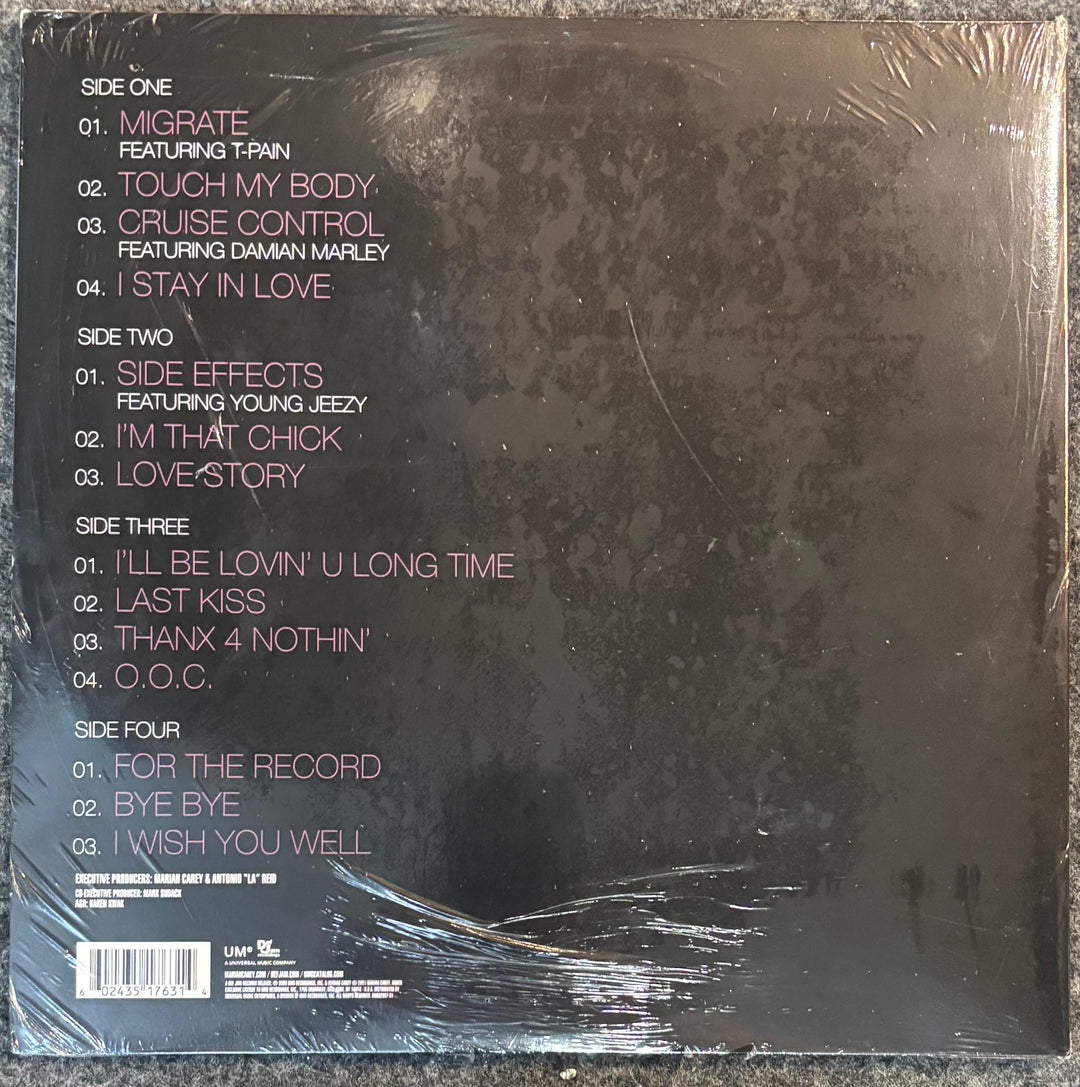The back cover of Carey, Mariah - E=mc2', wrapped in clear plastic. The cover is dark textured black with pink and white text listing the track titles and artists.