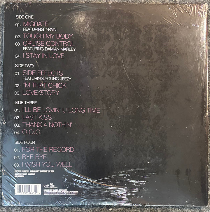 The back cover of Carey, Mariah - E=mc2', wrapped in clear plastic. The cover is dark textured black with pink and white text listing the track titles and artists.
