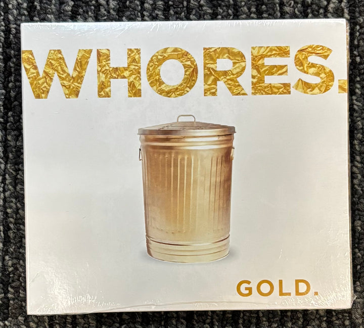 cd digipak packaging with a trash can and text 'WHORES. GOLD.' on a textured surface.