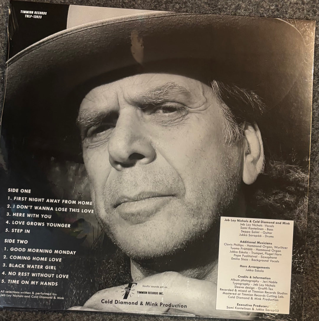 The back cover of Jeb Loy Nichols - This House Is Empty Without You, showing a black and white close-up portrait of the artist, track listings, and a white sticker card on a dark textured background.