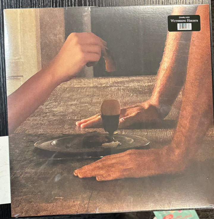 CHARLI XCX - WUTHERING HEIGHTS record cover with a person's hands at a table, possibly preparing food.