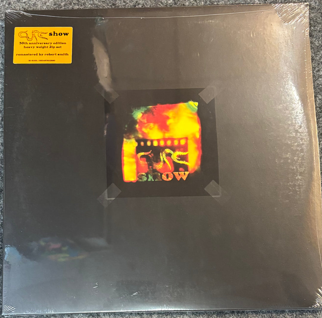 The Cure - Show record in packaging with a colorful label featuring text.