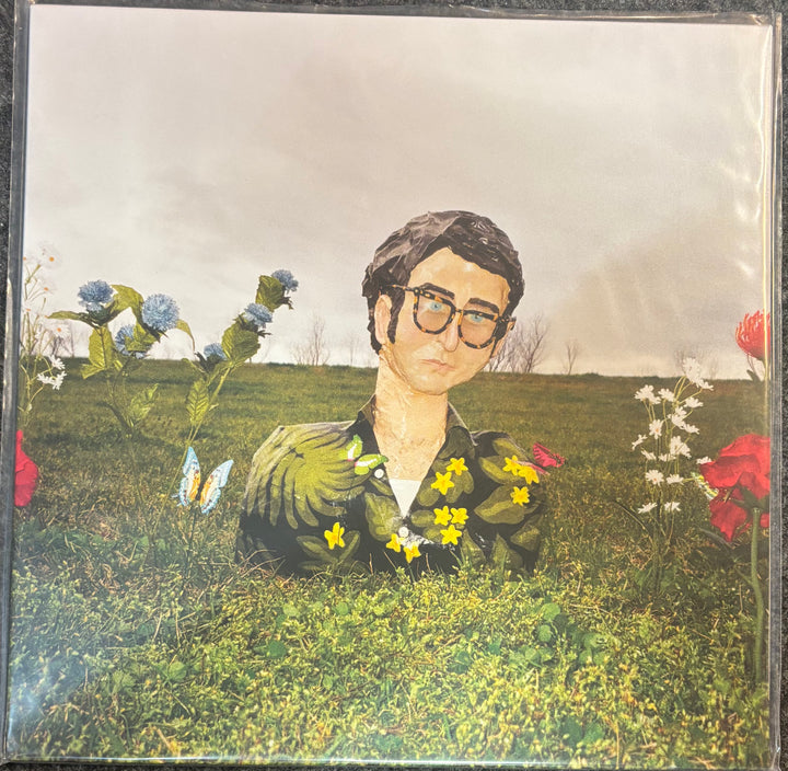 Album cover art for Max Bien Kahn – Flowers featuring a surreal illustration of a man in glasses sitting in a grassy field with flowers.