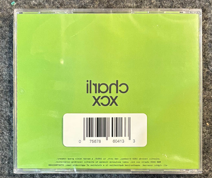 Charli XCX – Brat And It's Completely Different But Also Still Brat CD case with green back cover featuring a barcode and text on a textured surface