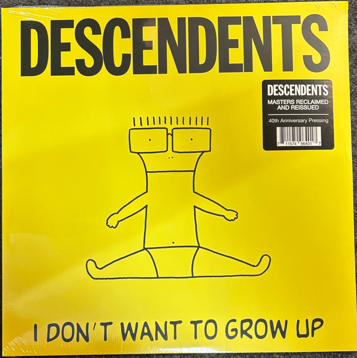 A bright yellow Descendents vinyl record cover for 'I Don't Want to Grow Up', featuring a simple black line drawing of a seated figure and a black sticker in the top right corner.