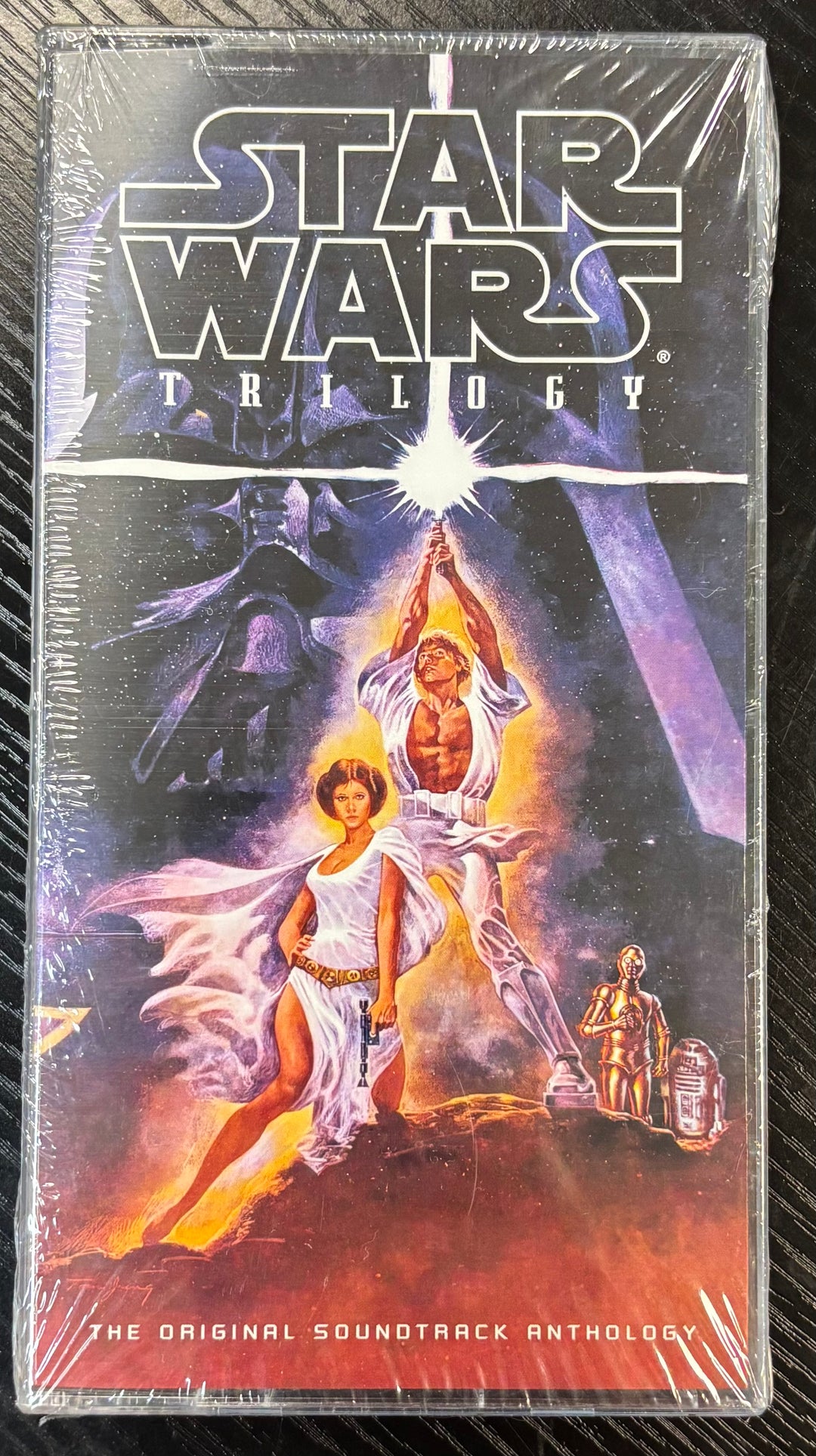 Cassette tape Box set  cover of 'Star Wars Trilogy' Soundtrack with characters and lightsaber on a dark background