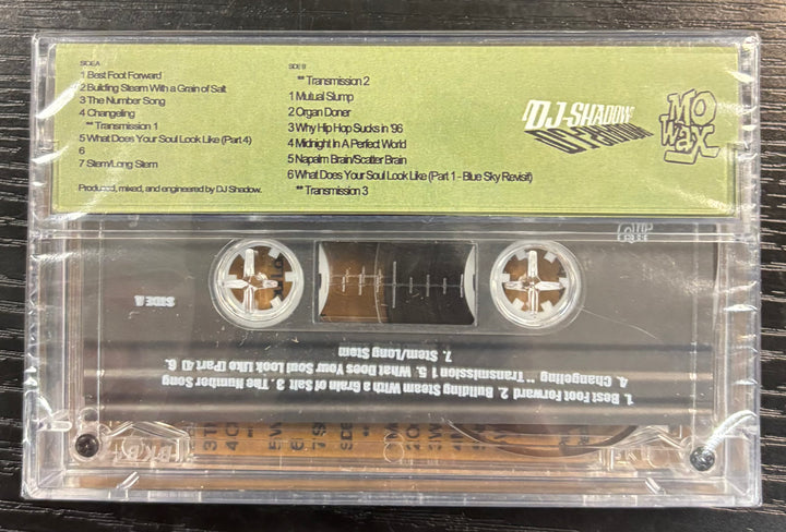 DJ Shadow – Endtroducing... DJ Shadow Cassette tape with a clear cover displaying text and branding on a wooden surface.