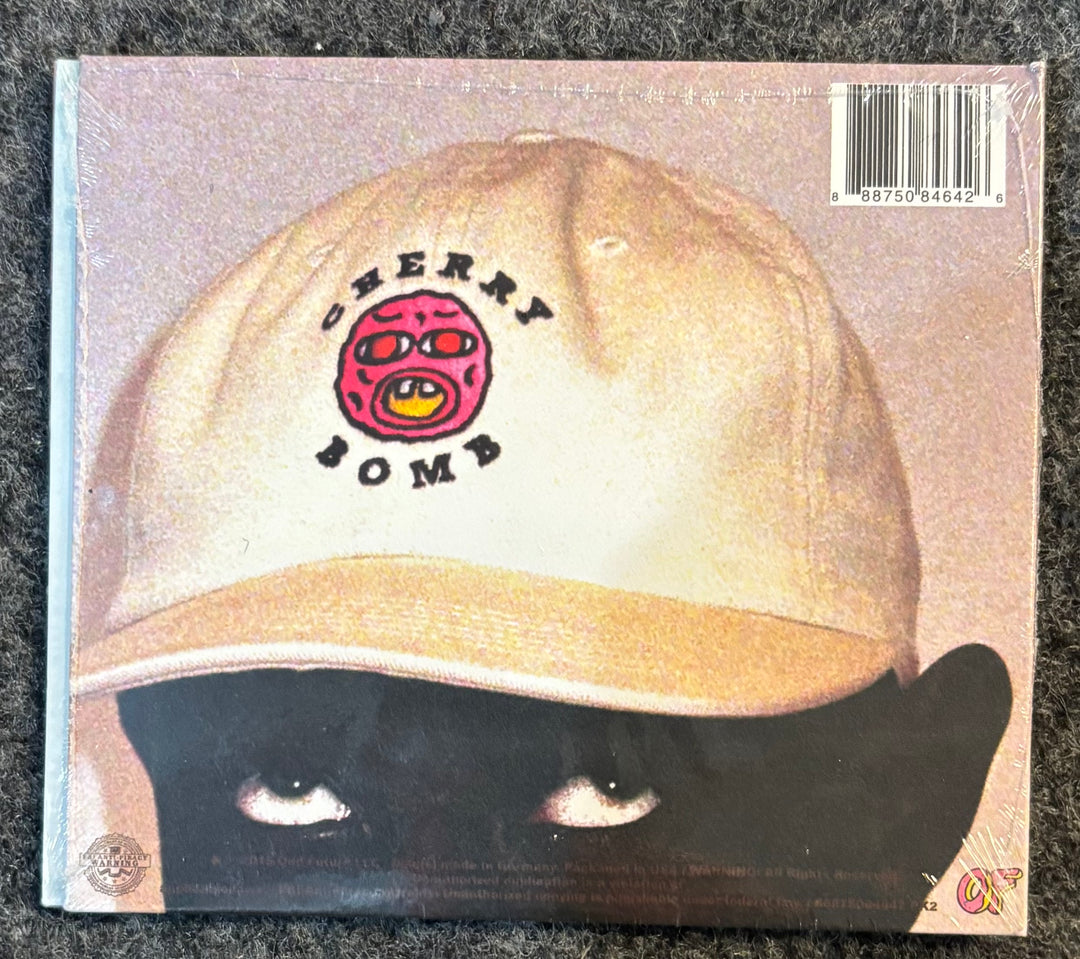 TYLER, THE CREATOR – cherry bomb cd back cover with a beige cap featuring 'Cherry Bomb' logo and a black cat's face.