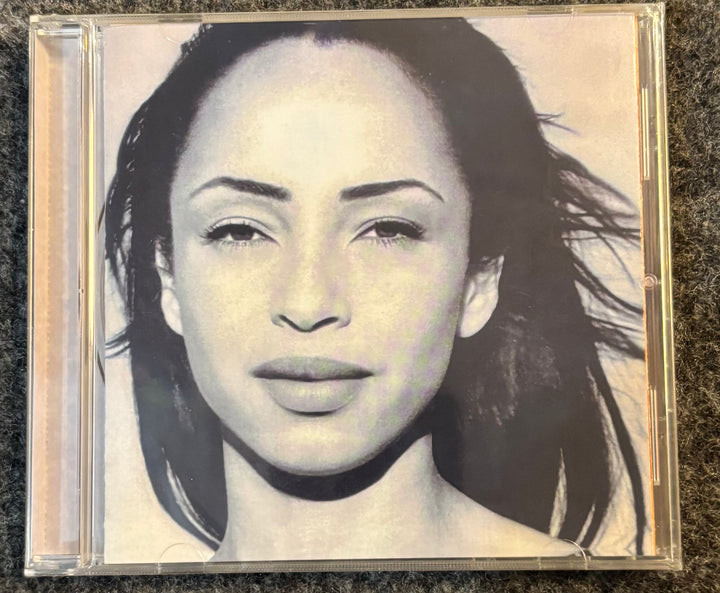 Sade - The Best Of Sade CD cover with a black and white portrait of a woman on a textured surface