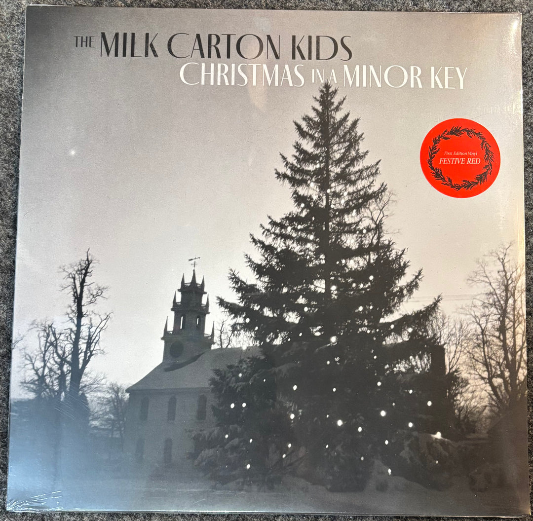 The Milk Carton Kids 'Christmas in a Minor Key' vinyl record cover, featuring a snowy winter scene with a church and a decorated Christmas tree. A red 'Festive Red' sticker is visible on the top right.