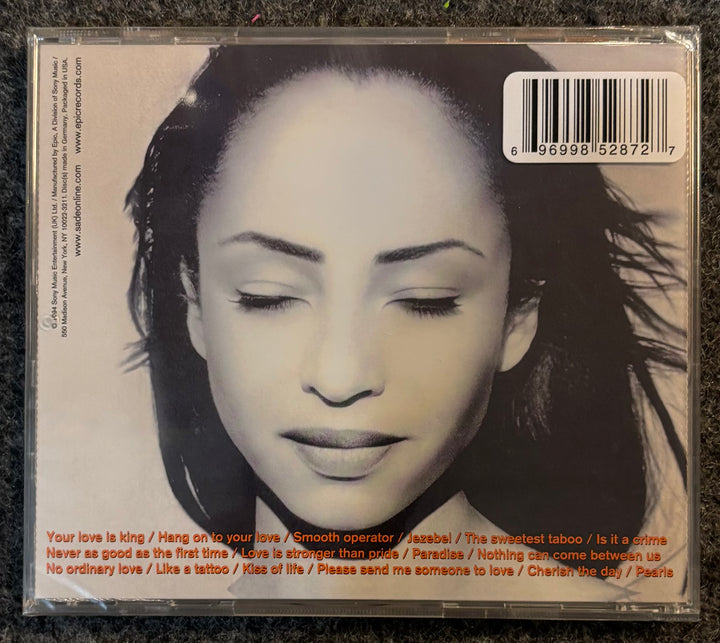 Sade - The Best Of Sade CD back cover with a black and white portrait of a woman and text on a dark surface