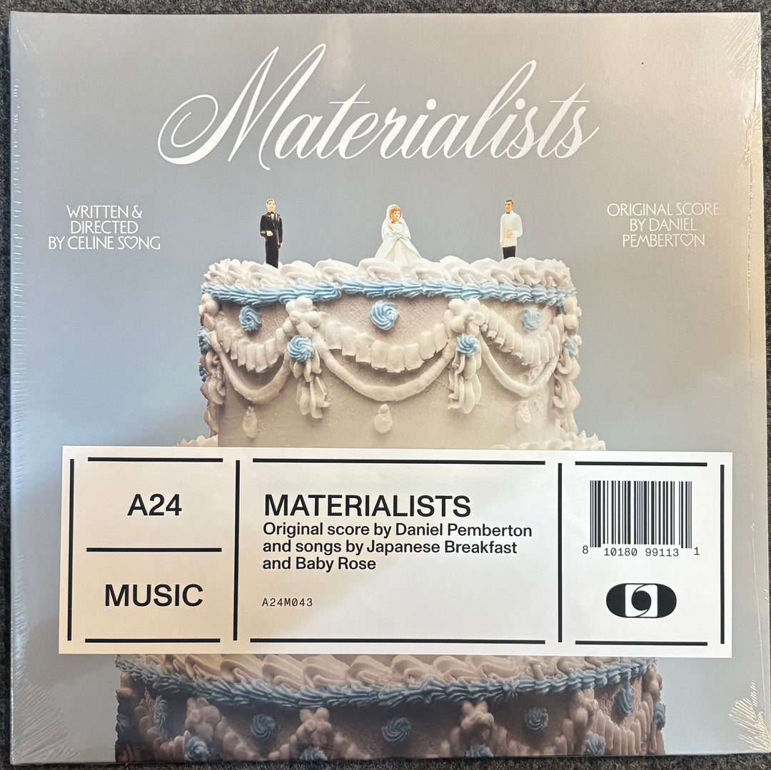 A24 Music 'Materialists' soundtrack album cover, featuring a white wedding cake with miniature bride and groom figures on top, with a white barcode label overlay at the bottom.