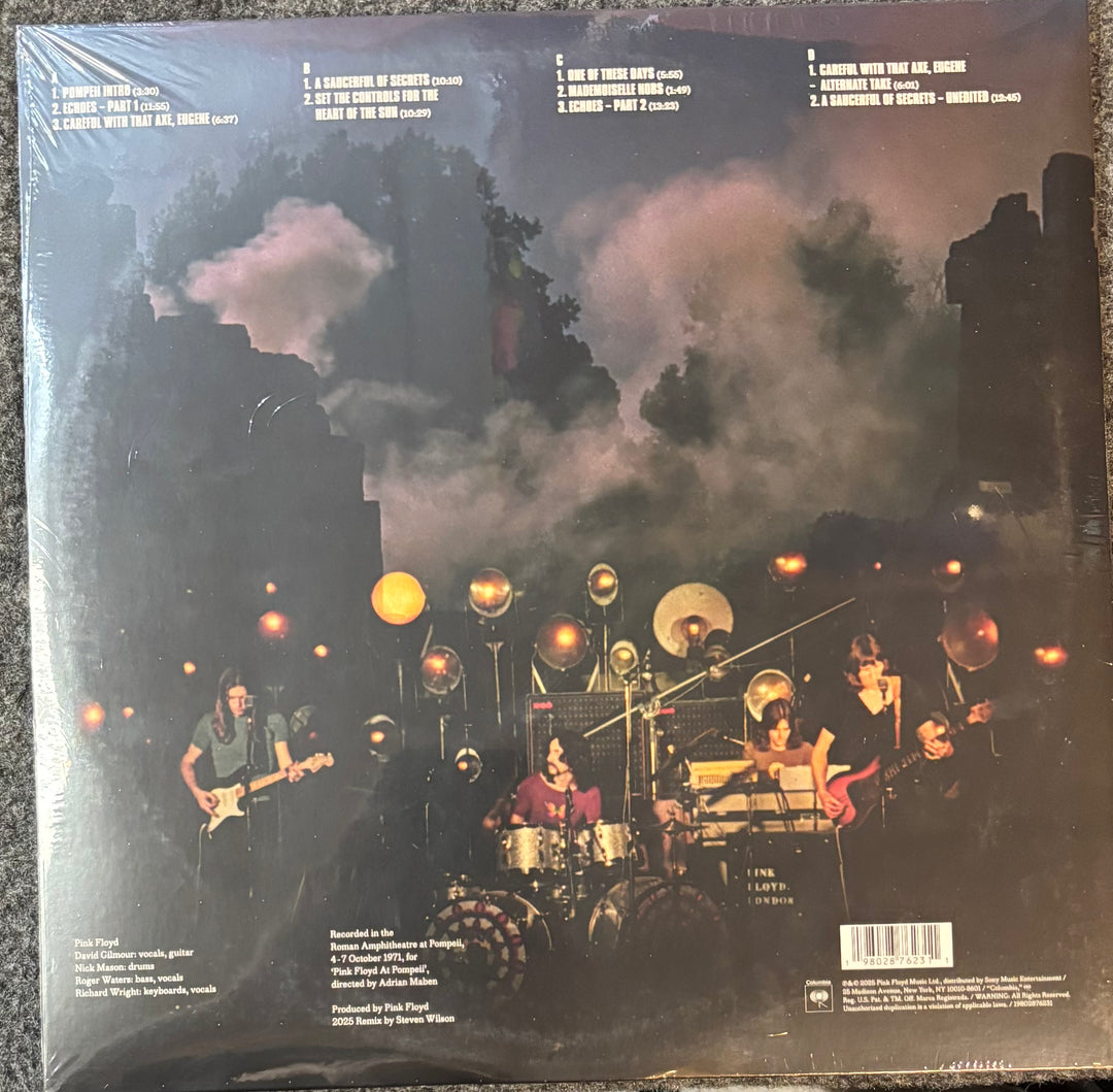 Pink Floyd – Pink Floyd At Pompeii-Mcmlxxi record cover with a band performing on stage under a dark sky with clouds.