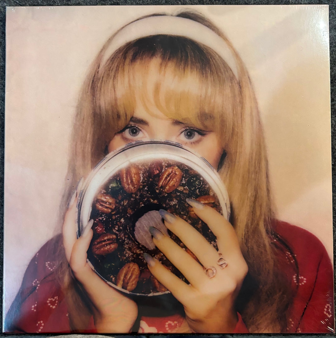 CARPENTER, SABRINA – FRUITCAKE (OLIVE GREEN VINYL) w/Person holding a round container with a spoon and nuts, wearing a headband and red top.