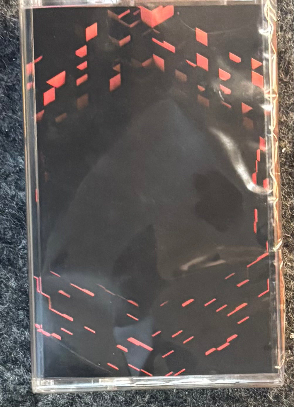 C418 - Minecraft Volume Beta cassette-style case or sleeve with red geometric dash patterns, photographed on a dark textured surface.