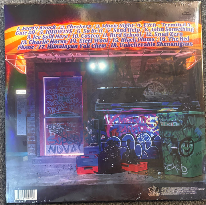 The back cover of Aesop Rock - Black Hole Superette, featuring a dark, graffiti-covered street scene with a bus and trash cans under a bright orange tracklist banner at the top.