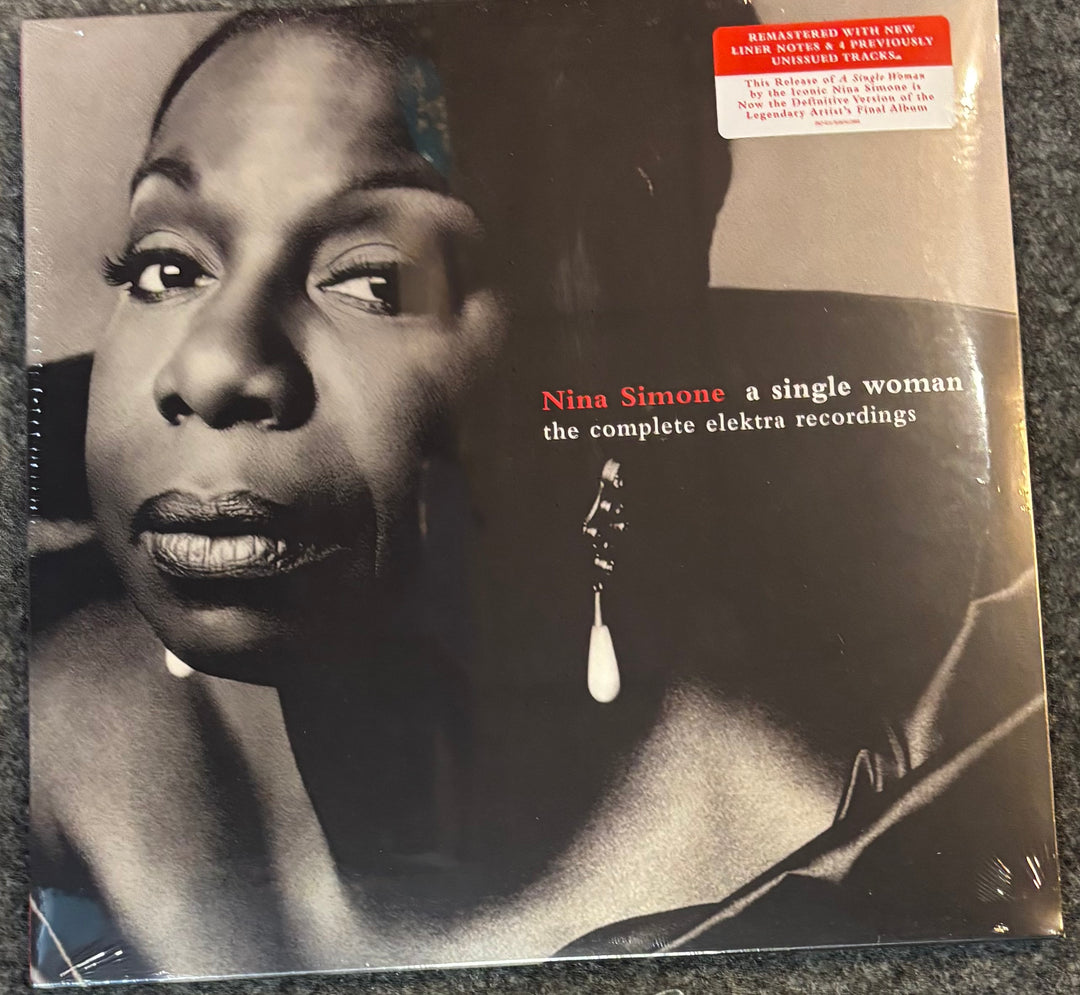 Vinyl record album cover for Nina Simone's 'a single woman the complete elektra recordings', featuring a black-and-white close-up portrait and a red remastered sticker at the top right, photographed on a dark textured surface.