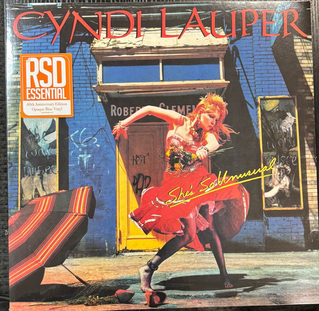 Cyndi Lauper - She's So Unusual cover featuring a person in a red dress dancing in front of a building with 'Cyndi Lauper' at the top.