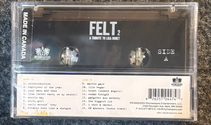A cassette tape of Felt's 'A Tribute to Lisa Ray' in a clear plastic case, showing the black cassette body, white text, and the back cover tracklist on a dark textured background.