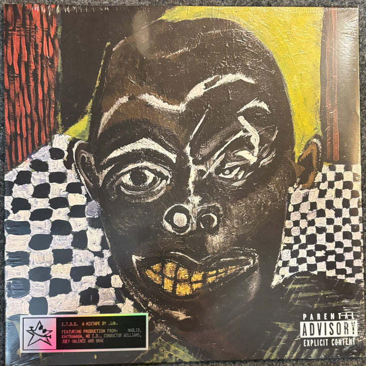 IDK – Even The Devil Smiles vinyl record sleeve featuring a stylized, textured portrait of a face in black, white, yellow, and red. The sleeve includes a pink and green label at the bottom left and a Parental Advisory label at the bottom right.