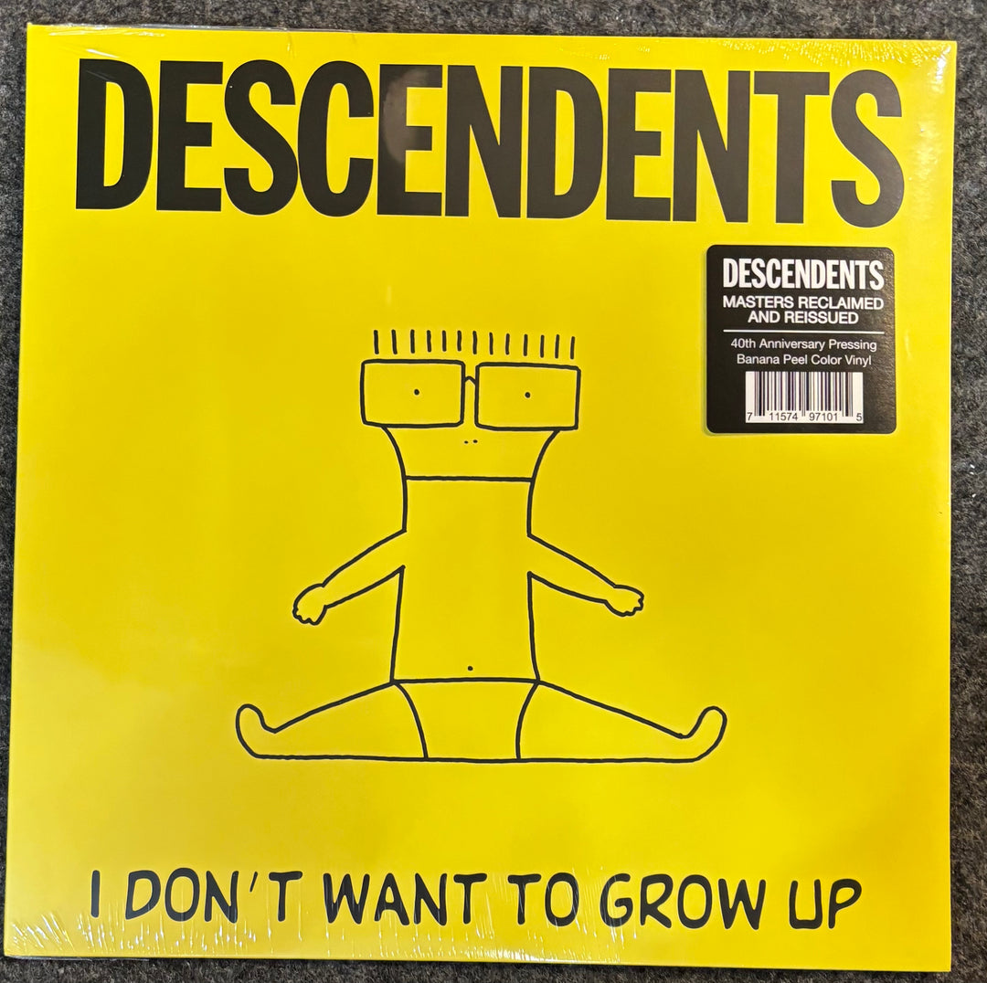 A vinyl record sleeve for the band Descendents, featuring a bright yellow background with bold black text reading 'DESCENDENTS' at the top and 'I DON'T WANT TO GROW UP' at the bottom. A simple black line drawing of a seated figure with glasses is centered on the cover, and a black 'Descendents Masters Reclaimed and Researched 40th Anniversary Pressing Variant Pink Color Vinyl' sticker is in the upper right.