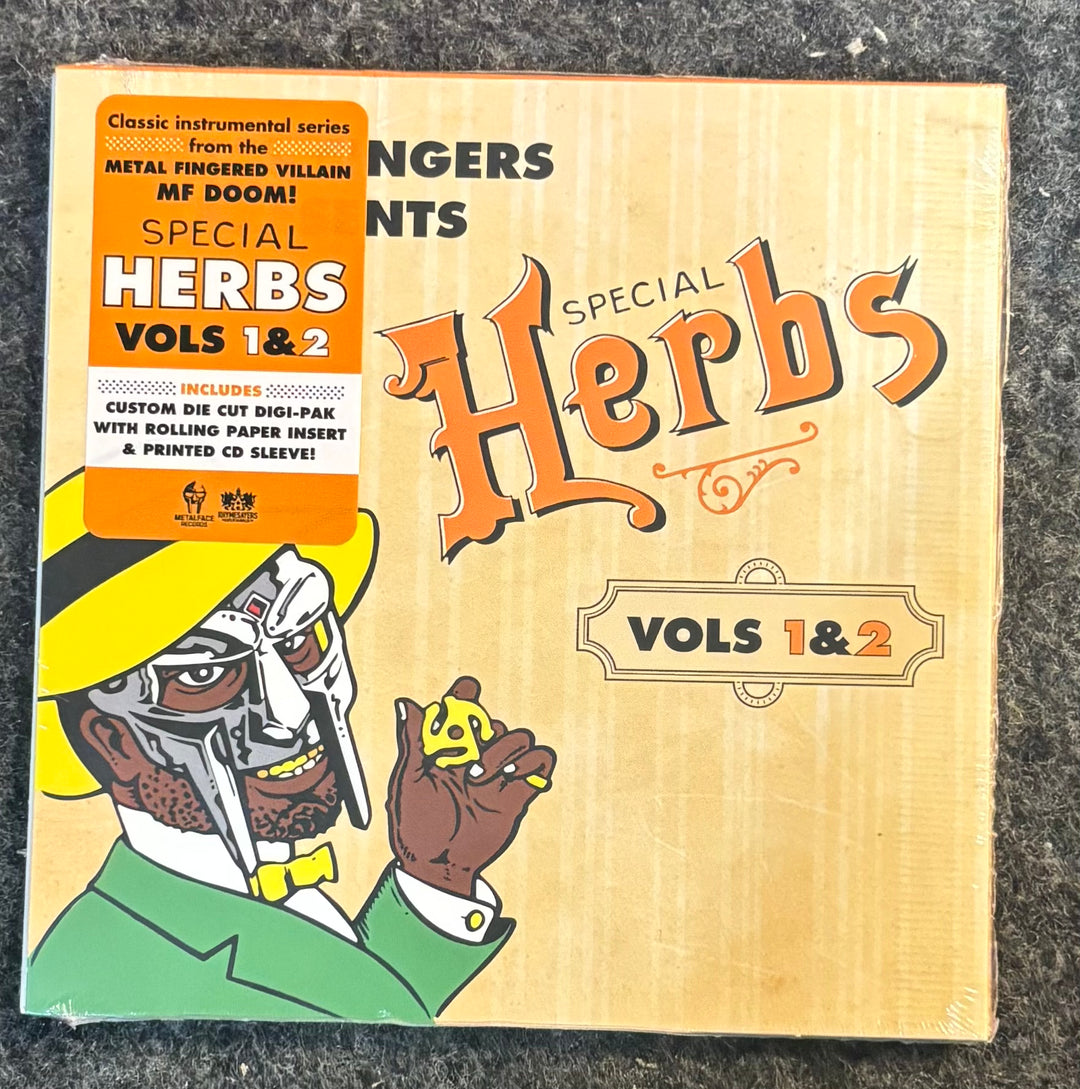 Metal Fingers (MF DOOM) - Special Herbs Vol. 1 & 2. The packaging features a light wood-grain background with orange gothic lettering, an orange sticker on the left, and an illustration of a cyborg character in a yellow hat and green suit holding a small yellow mushroom.