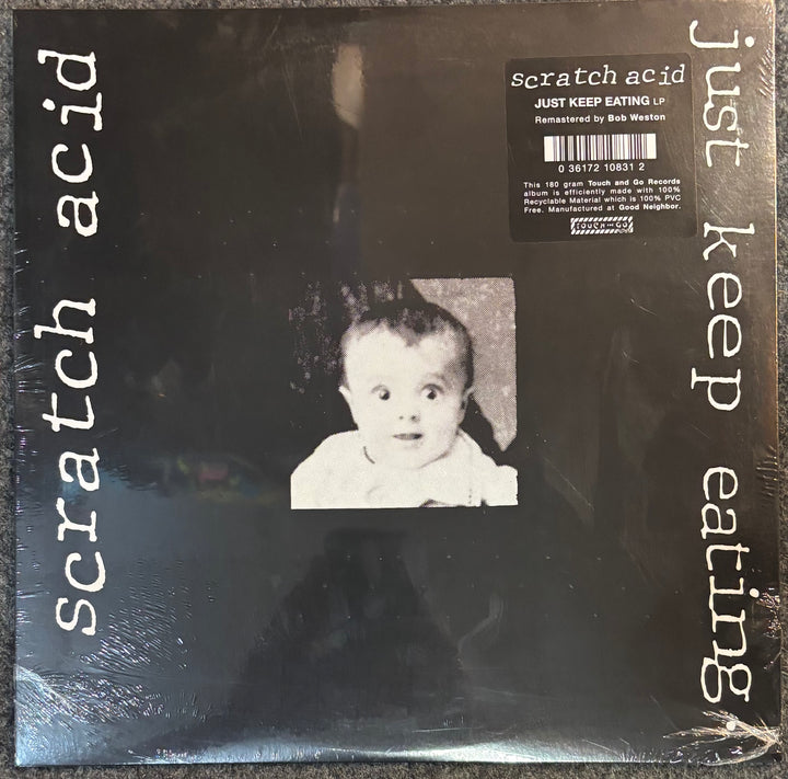 A vinyl record sleeve for the band 'scratch acid' and their album 'just keep eating'. The cover is black with white text running vertically on the left and right sides, and a black-and-white photo of a surprised baby in the center.