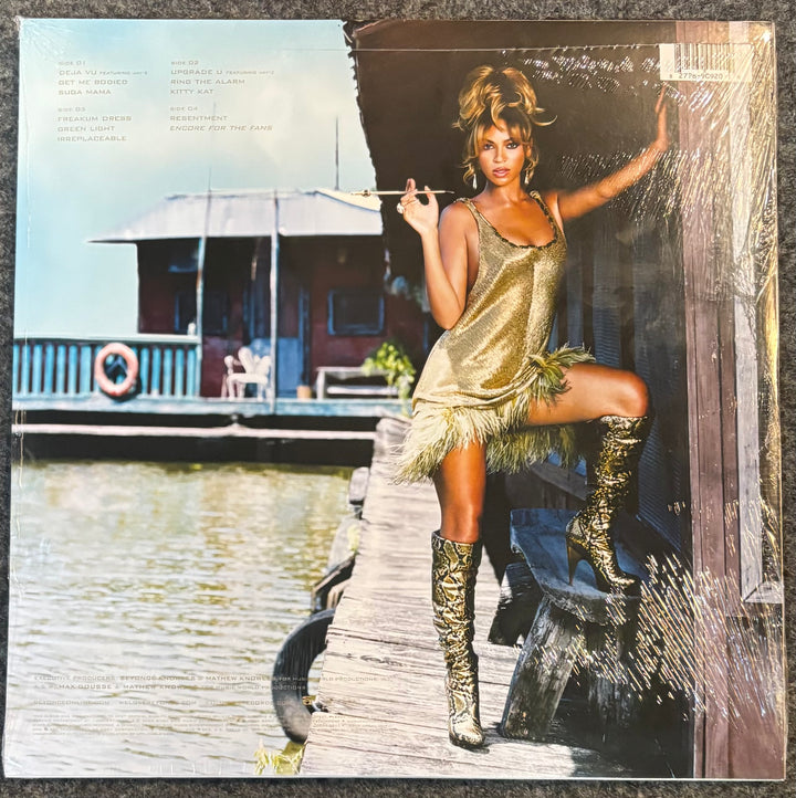 A vinyl record sleeve for Beyonce - B'day featuring a color photograph of a woman posing on a wooden dock wearing a gold fringed dress and matching boots, with a house and water in the background.