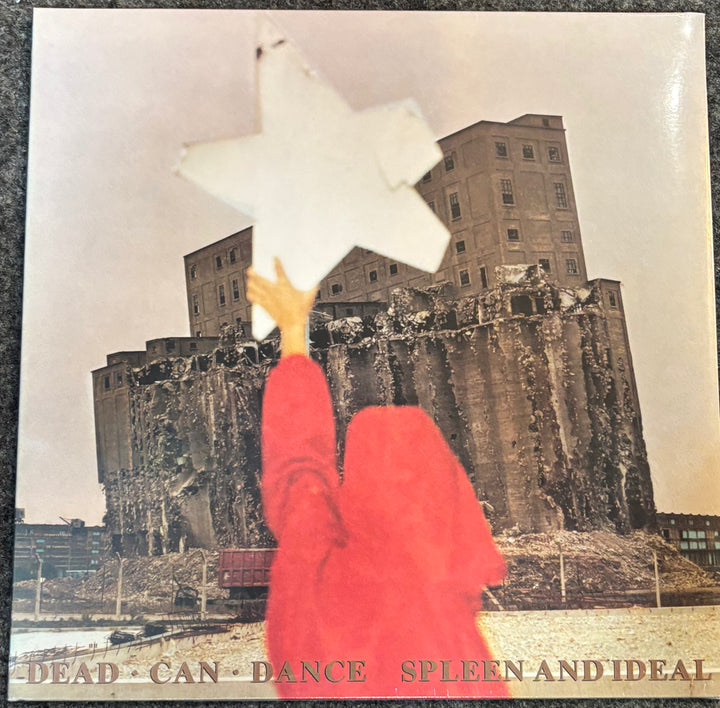 Dead Can Dance - Spleen And Ideal Album cover with a person in a red coat holding a star above a large building.