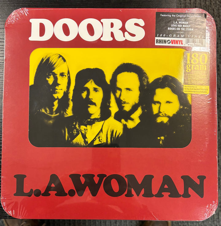 Vinyl record cover for 'L.A. Woman' by The Doors with a red background and black and yellow portrait of the band members.