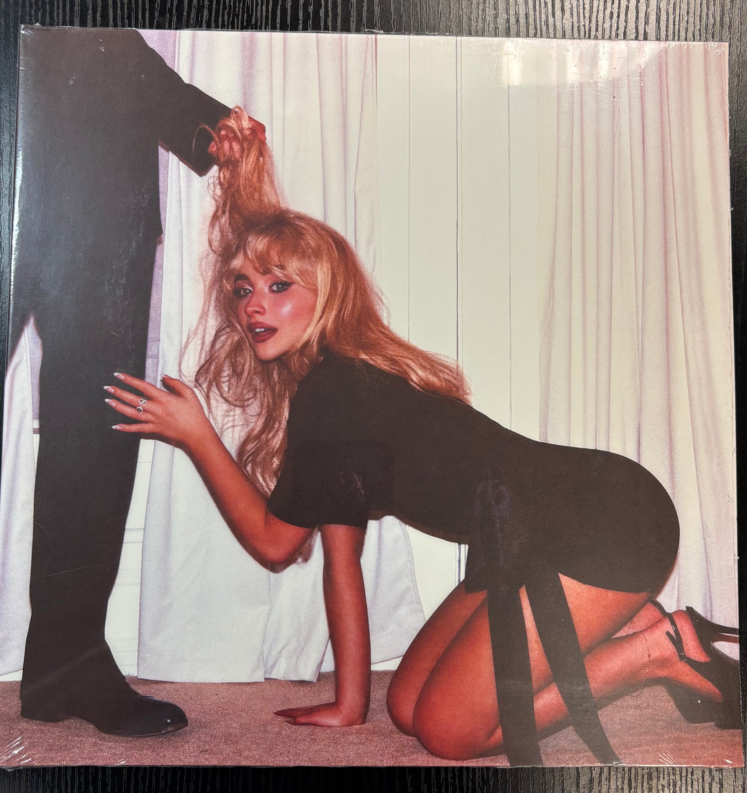 Sabrina Carpenter vinyl record cover with a woman in a black outfit kneeling and a man's leg in the foreground.