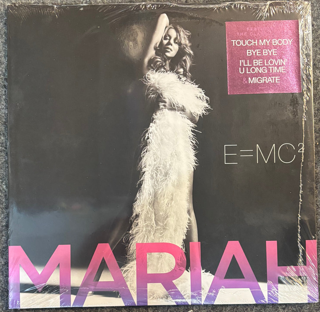 A vinyl record sleeve for Mariah's album 'E=MC²' in its shrink wrap, featuring a black background with a model in a white feathered dress and pink gradient text.