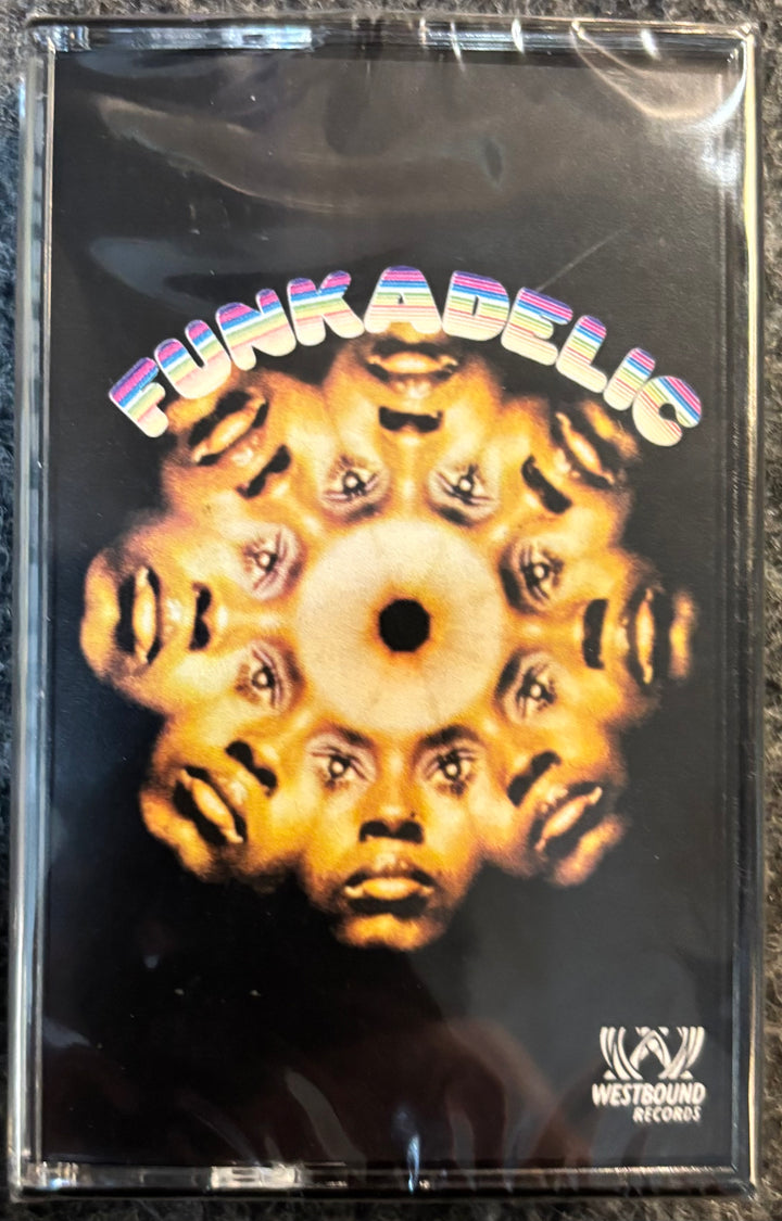 A cassette tape of Funkadelic - Funkadelic, sealed in its original clear plastic shrink wrap. The cover art features a central circular motif with multiple stylized faces radiating outward on a black background, with the band's name 'FUNKADELIC' written in a colorful, wavy font at the top.