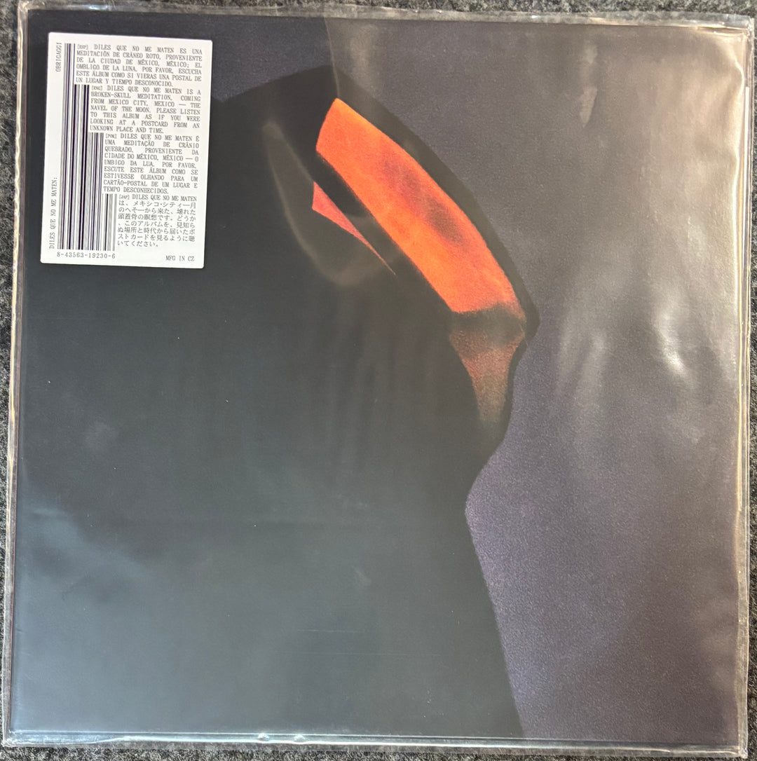 A vinyl record sleeve for Obrigaggi – Diles Que No Me Maten, featuring a dark silhouette with a bright orange glowing eye on a black background. A white barcode sticker is visible in the top-left corner.
