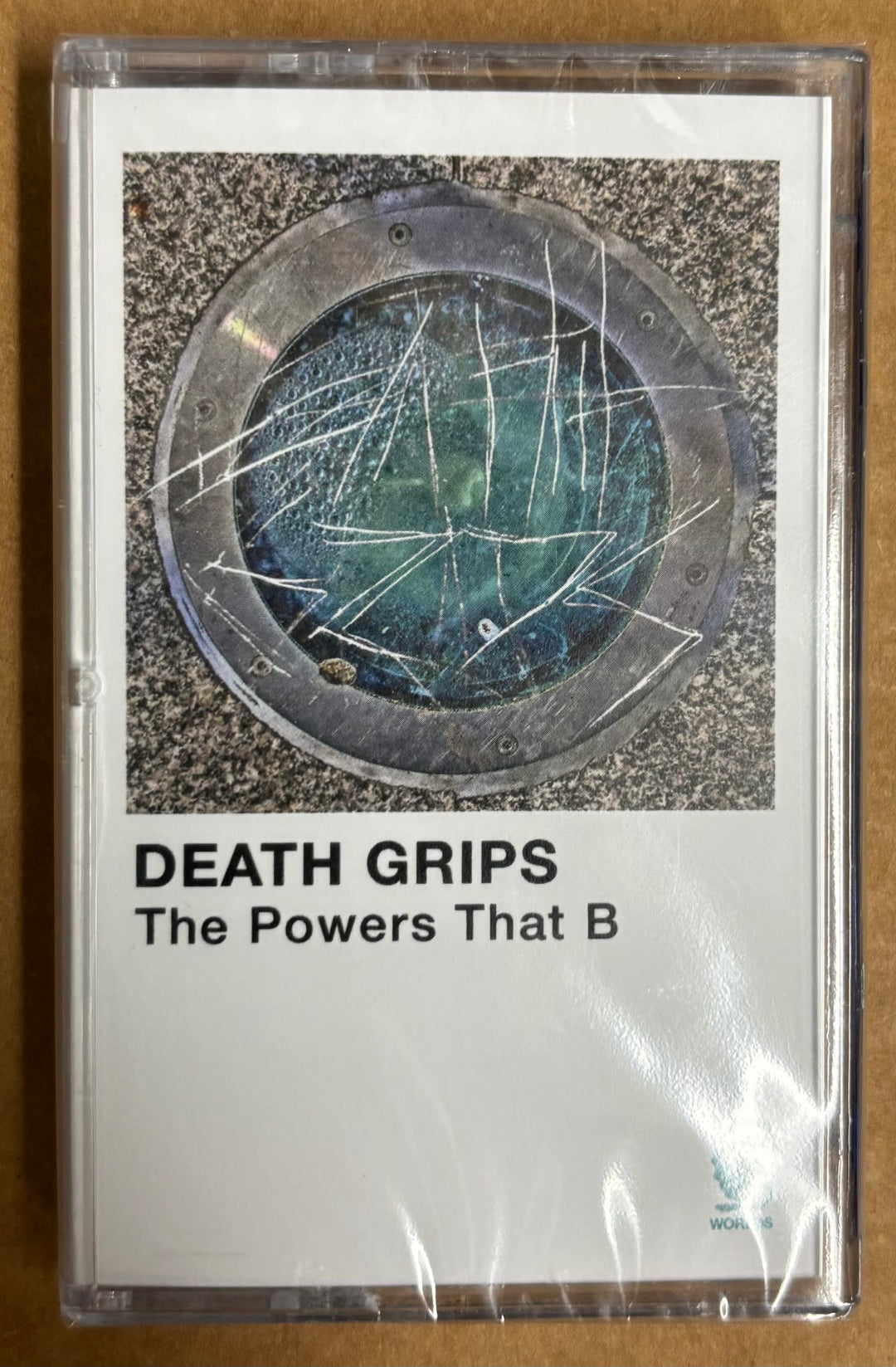 Cassette tape with 'Death Grips' album cover featuring a broken glass design on a textured surface.