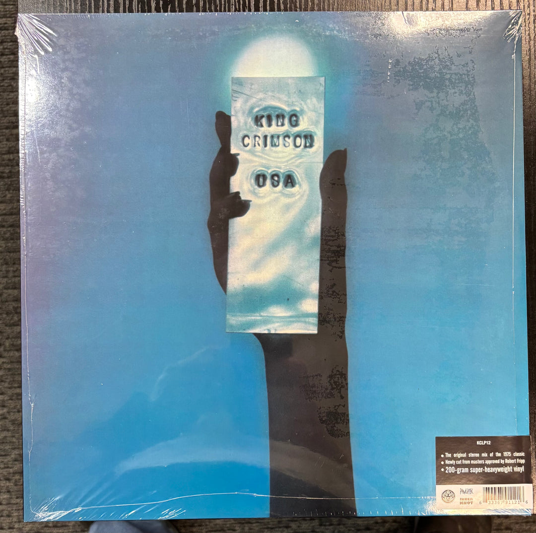 KING CRIMSON – USA record cover with a hand holding a card displaying 'King Crimson' on a blue gradient background.