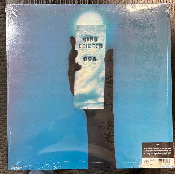 KING CRIMSON – USA record cover with a hand holding a card displaying 'King Crimson' on a blue gradient background.