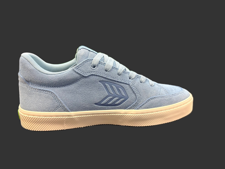 Blue sneaker with white sole on a black surface, with a blurred background
