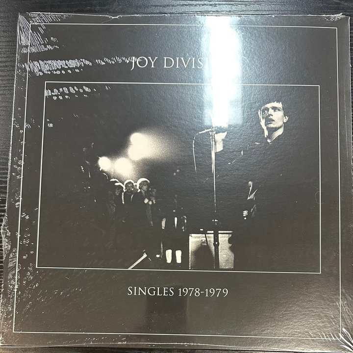 Joy Division album 'Singles 1978' on a vinyl LP record, with a black and white cover featuring a photo of the band performing.
