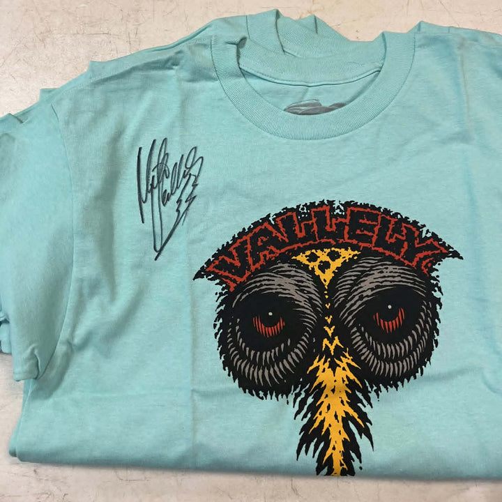 A light blue t-shirt featuring a large graphic of an owl with red eyes and a yellow beak, under a red and black 'VALLEY' banner. A black script signature is printed on the left chest.