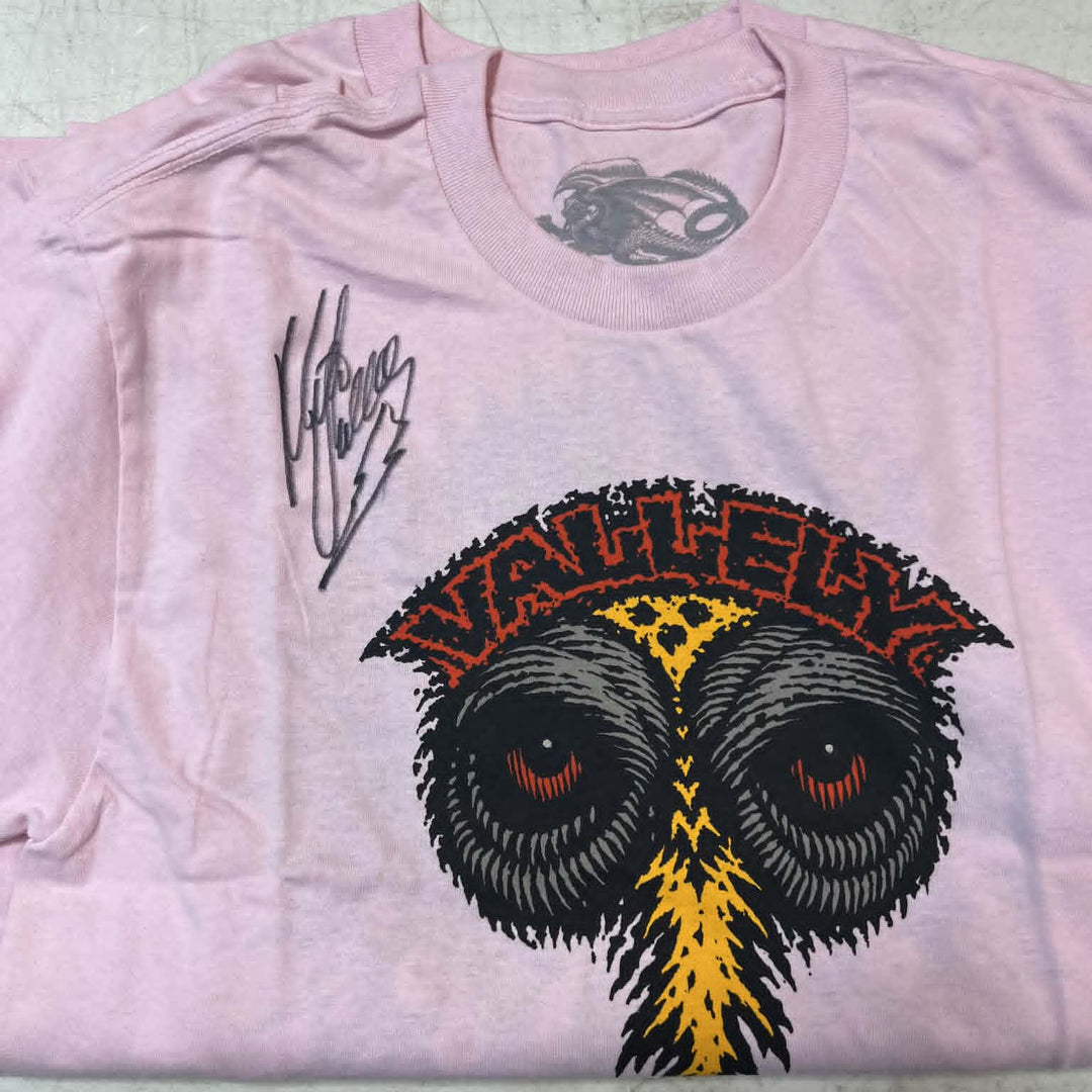 A light pink short-sleeve t-shirt featuring a large graphic of an owl with red eyes, a yellow beak, and a red-and-black patterned crest with the word 'Vanity'. A black script signature is printed on the left chest.